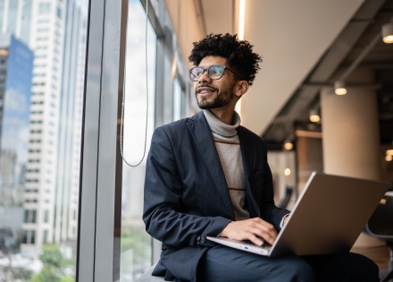 Employee sitting on window sill with laptop at office