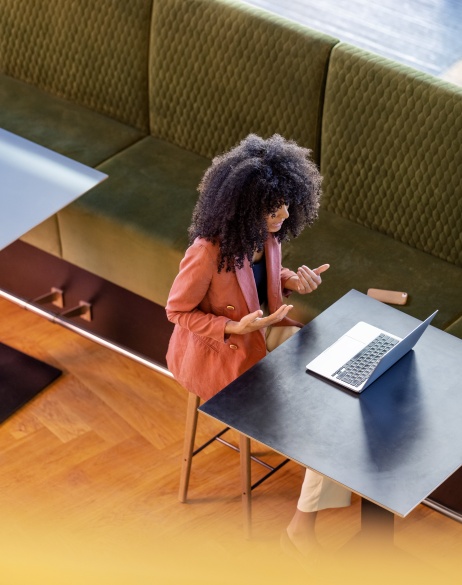 Overhead view of woman on laptop meeting, sitting at table in open space.