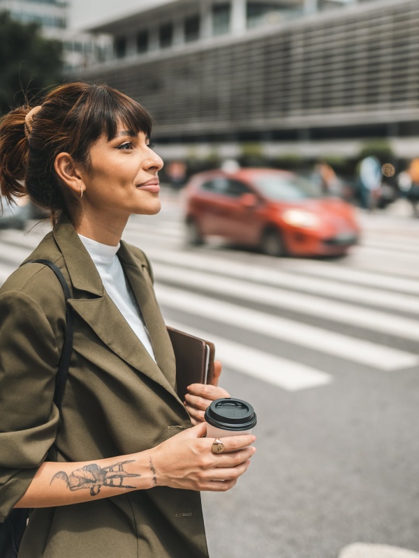 A woman crossing the street with a coffee, considering Brazil EOR services.