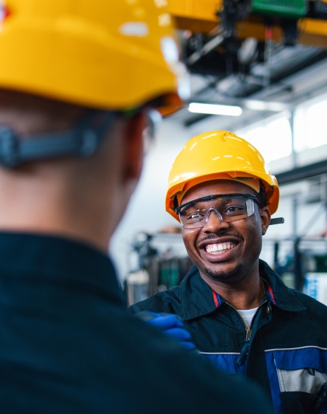 Three male colleagues wearing construction hats and safety glasses indoors.