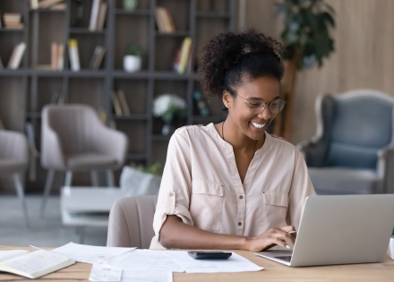 Smiling young woman reading about payroll taxes in Jamaica on her laptop