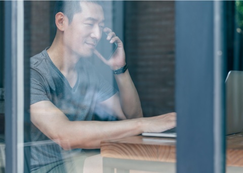 A business owner talking on his mobile phone and working on his laptop from a public workspace in the People’s Republic of China